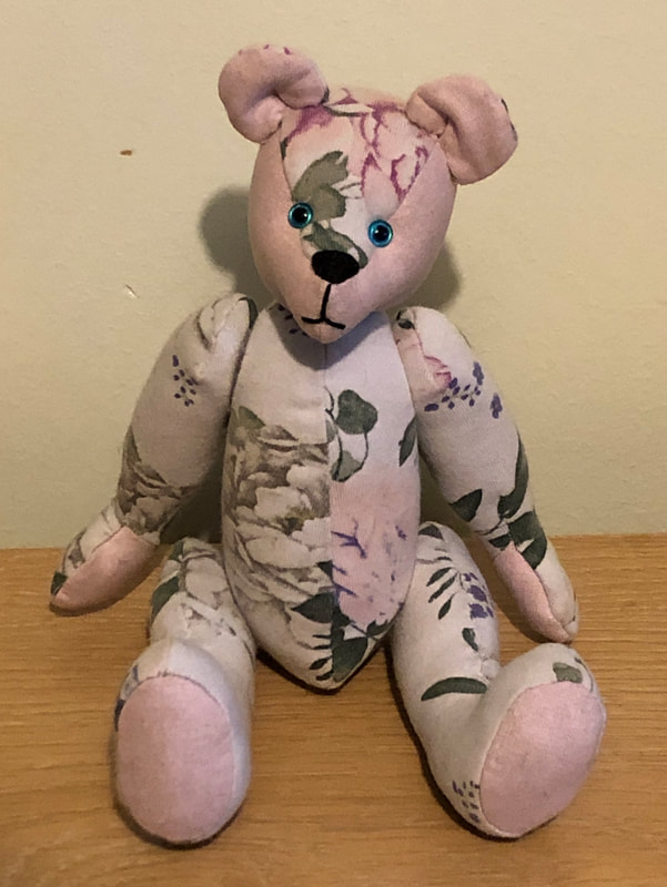 White & pink floral teddy bear with blue eyes. Made from a baby's romper suit.